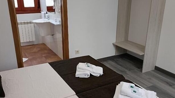A hotel room with a bed, a TV mounted on the wall, a bathroom visible through an open door, and a coat rack. - Albergue Miraiso (Arzua)