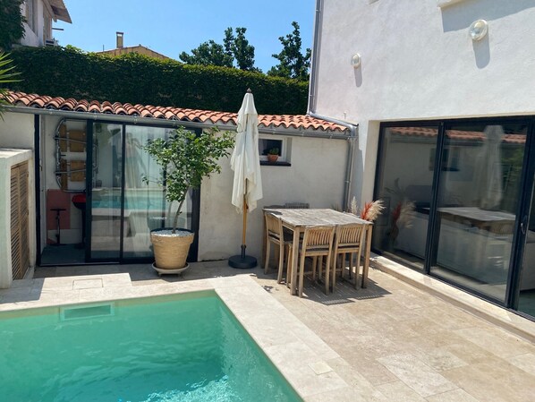 Un área de piscina con un suelo de baldosas, una mesa de madera con sillas y una planta en maceta.