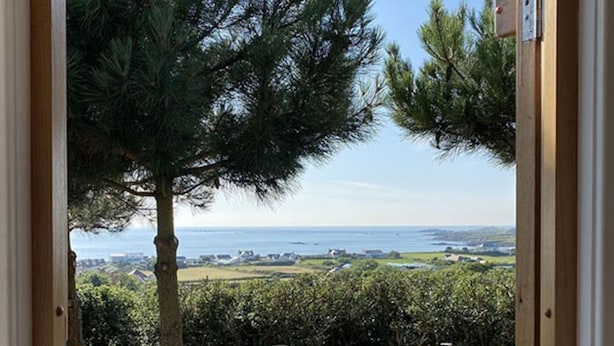Una terraza de madera con mesa y sillas, con vistas a un paisaje costero con árboles y el mar.
