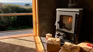 Una habitación acogedora con una estufa de leña, un ventanal con vistas panorámicas y varios regalos envueltos en el suelo.