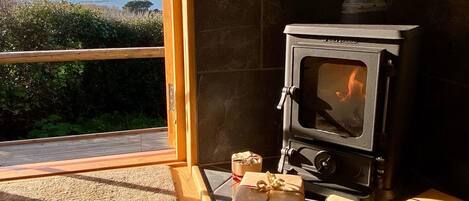 A cozy room with a wood-burning stove, a large window overlooking a scenic view, and several wrapped gifts on the floor.