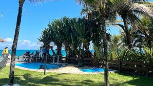A pool area with palm trees, a wooden fence, and a clear blue sky. - Pousada Mar a Vista (Ipojuca)