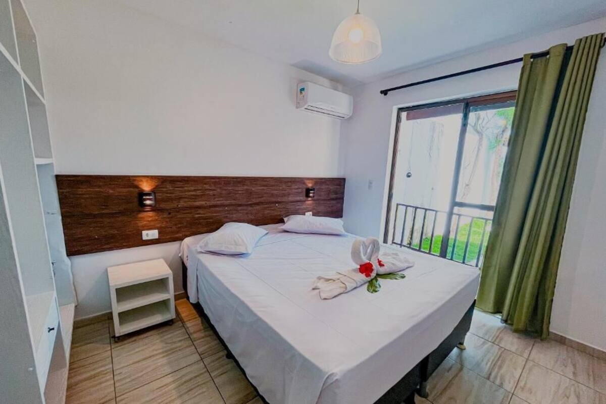 Habitación de hotel con cama, mesita de noche, aire acondicionado instalado en la pared y vista al exterior.