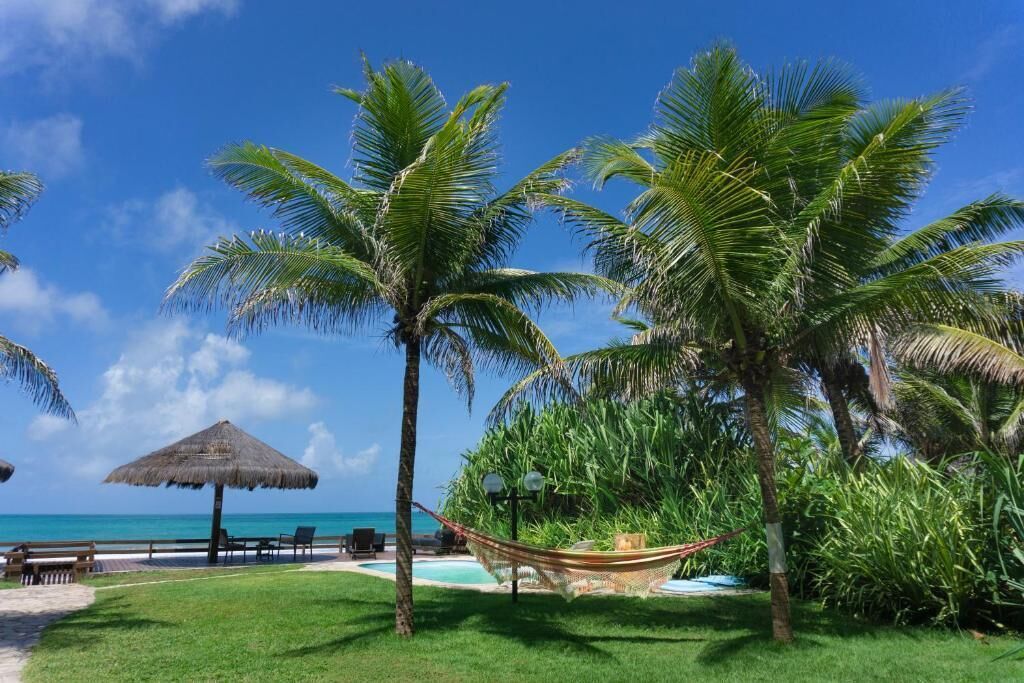 A tropical resort with palm trees, a hammock, a thatched umbrella, and a pool area.