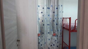Ein Zimmer mit Holzboden, einer weißen Tür, einer Dusche mit blumigen Vorhängen und einem roten Etagenbett.
