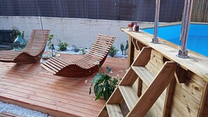 Une terrasse en bois avec deux chaises longues et une piscine.
