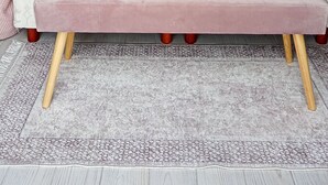 Une chambre à coucher avec une tête de lit capitonnée, une couvre-lit rose, deux serviettes enroulées, un banc et deux lampes fixées au mur.