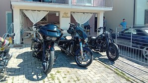 Un immeuble doté d’un balcon, avec deux motos garées devant, et une enseigne indiquant « Chambre d’hôtes ».