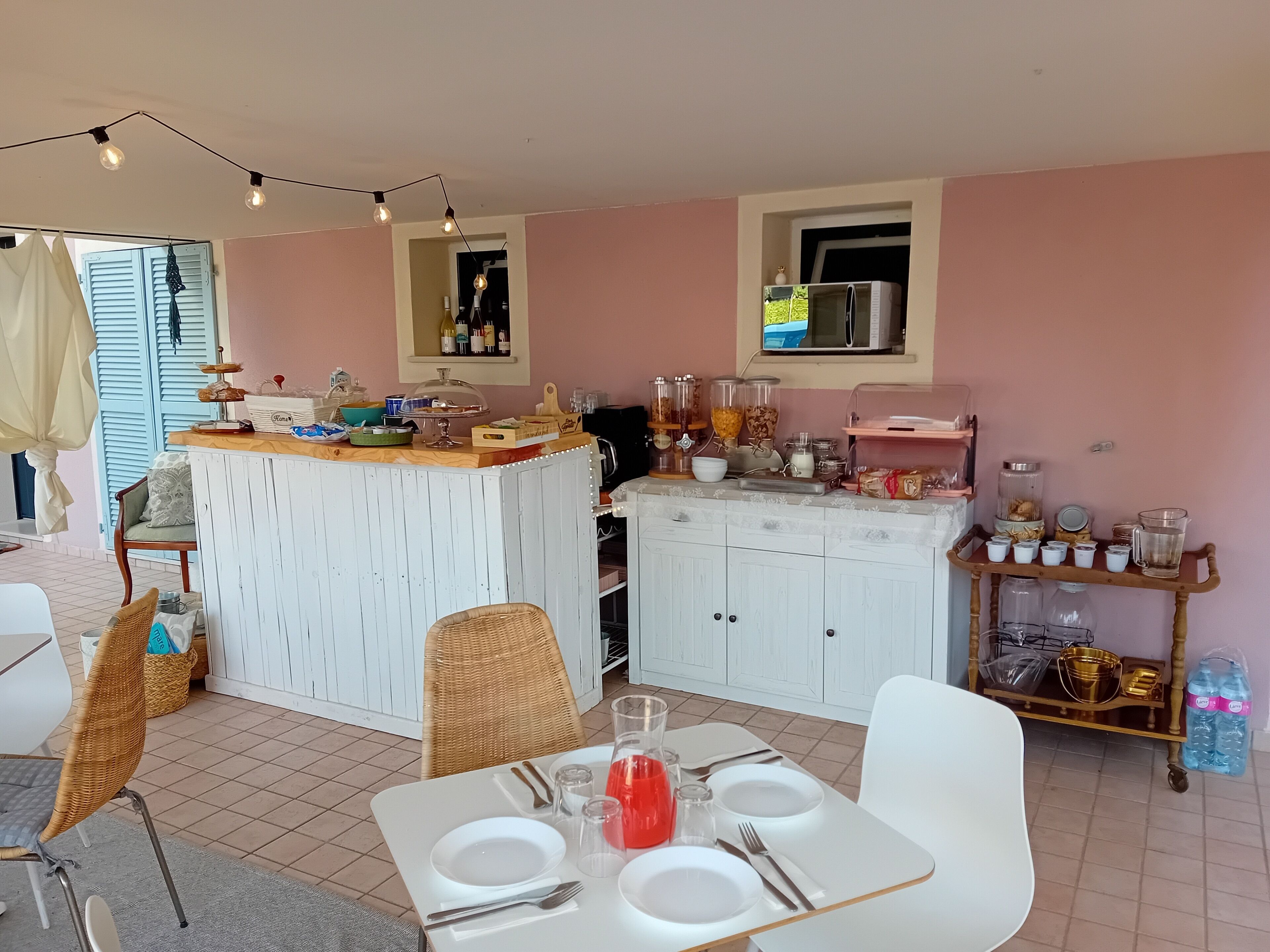 A dining area with a white table set for four, a buffet counter with various food items, and a kitchen area with cabinets and appliances.