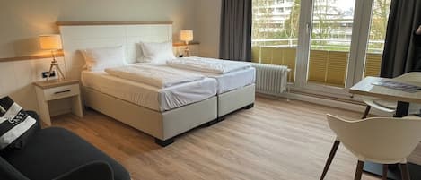 Habitación de hotel con cama, mesitas de noche, una silla, una pequeña mesa y vistas al exterior.