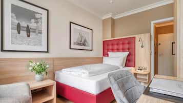 Habitación de hotel con cama, escritorio, silla, armario y dos cuadros en la pared.