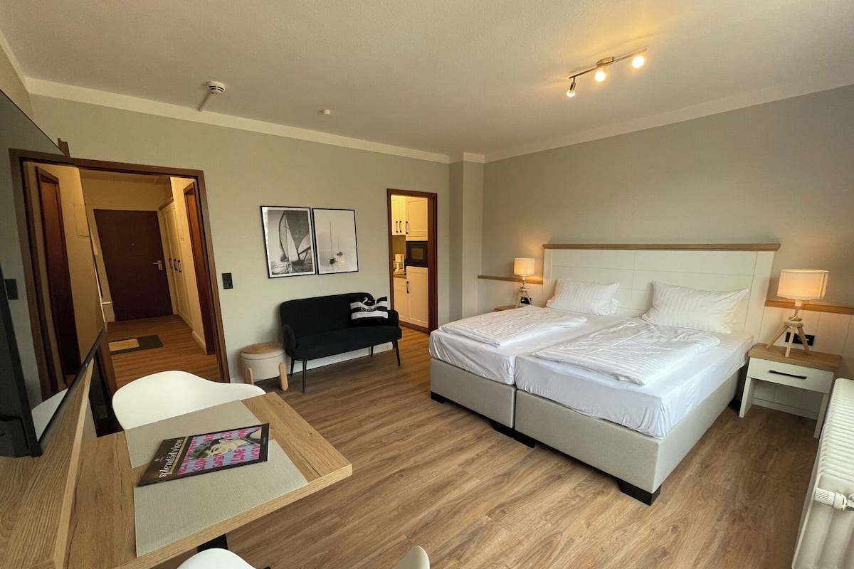 A hotel room with a bed, bedside tables, a desk, a chair, a sofa, and a small table with a book.