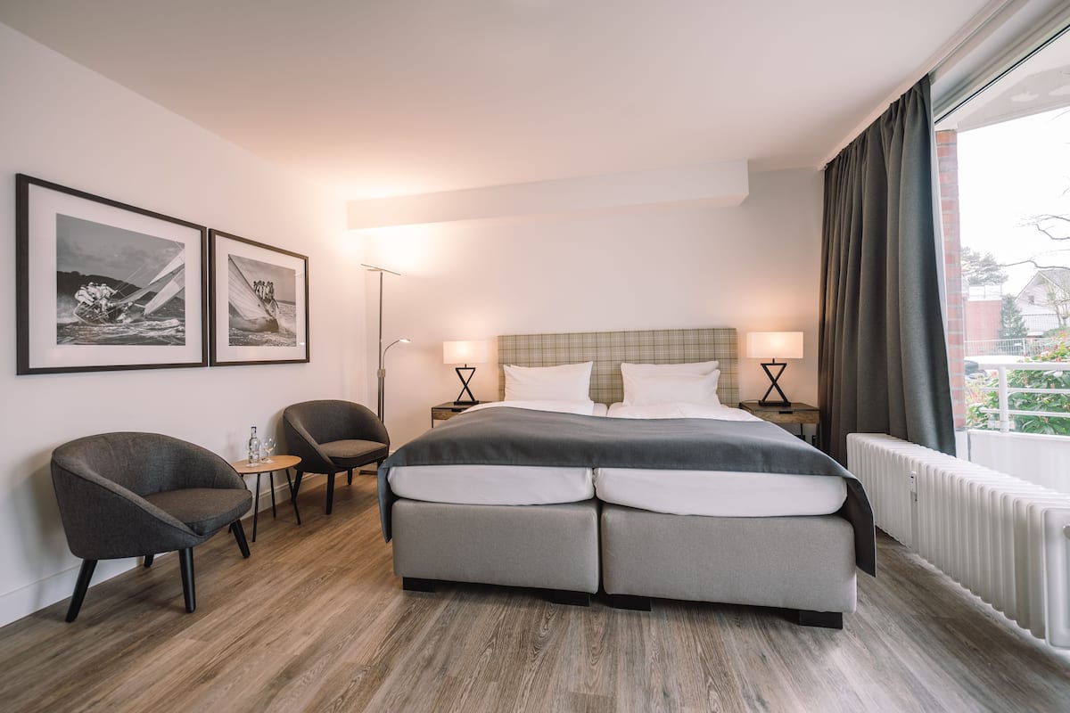 A modern hotel room with a large bed, two armchairs, a small table, and framed pictures on the wall.