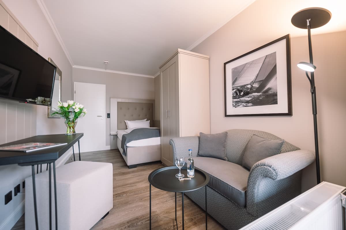 A modern hotel room with a bed, sofa, and a small table with a vase and glasses.