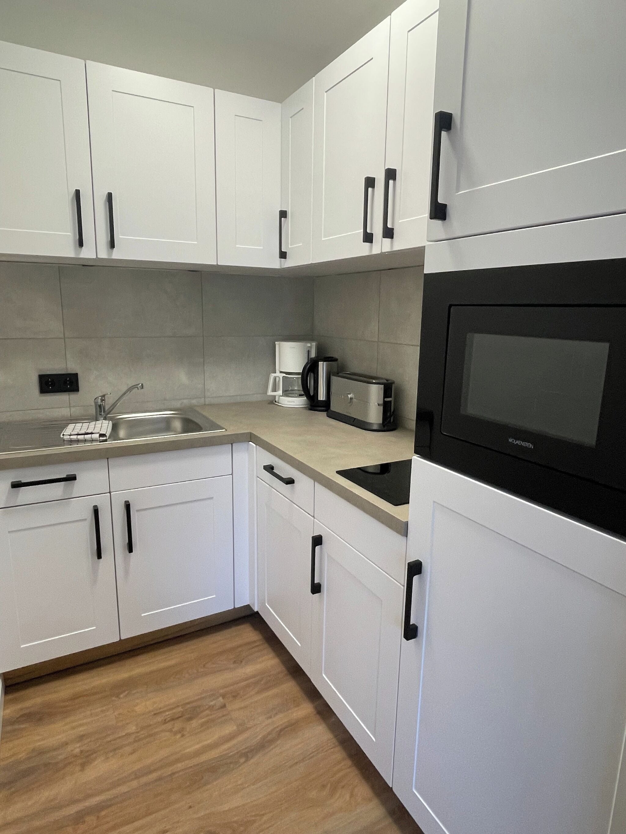 Una cocina moderna con armarios blancos, un lavamanos de acero inoxidable, una cafetera y un microondas.