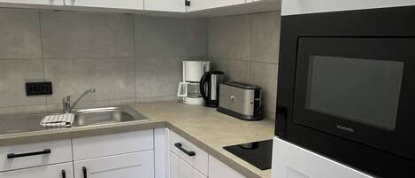 Una cocina moderna con armarios blancos, un lavamanos de acero inoxidable, una cafetera y un microondas.