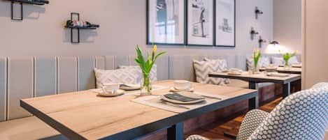 A dining area with a long wooden table, cushioned seating, and framed artwork on the wall.