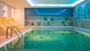 A swimming pool with yellow lounge chairs and a mural of a tropical landscape on the wall. - Hotel Royal - Timmendorfer Strand (Timmendorfer Strand)