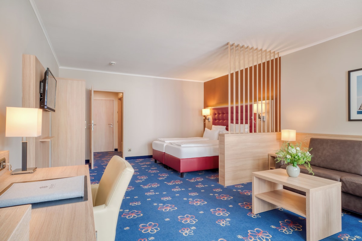 A hotel room with a bed, a desk, a chair, a sofa, and a decorative wall panel.