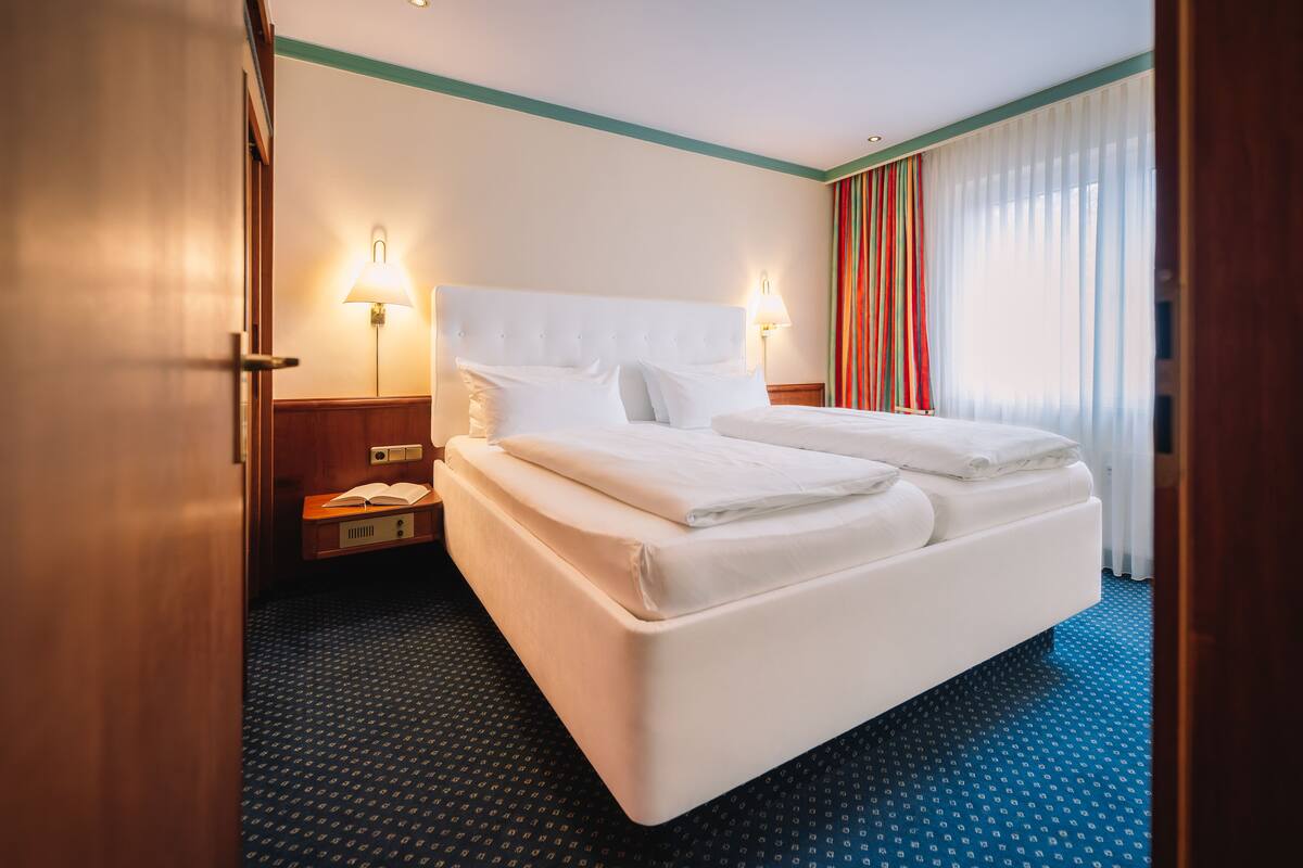 A hotel room with a large bed, two bedside lamps, a nightstand, and a window with curtains.