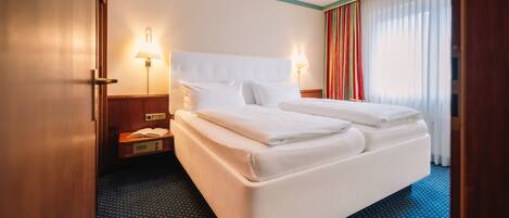 Habitación de hotel con una cama grande, dos lámparas de noche, una mesita de noche y una ventana con cortinas.