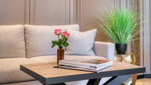 A modern living room with a sofa, a coffee table, a vase with pink roses, and a potted plant. - Hotel Royal - Timmendorfer Strand (Timmendorfer Strand)