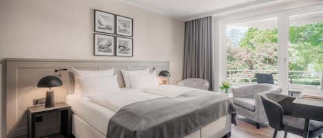 Une chambre d’hôtel moderne dotée d’un grand lit, de tables de chevet, d’un bureau avec une chaise et offrant une vue sur la verdure par la fenêtre.