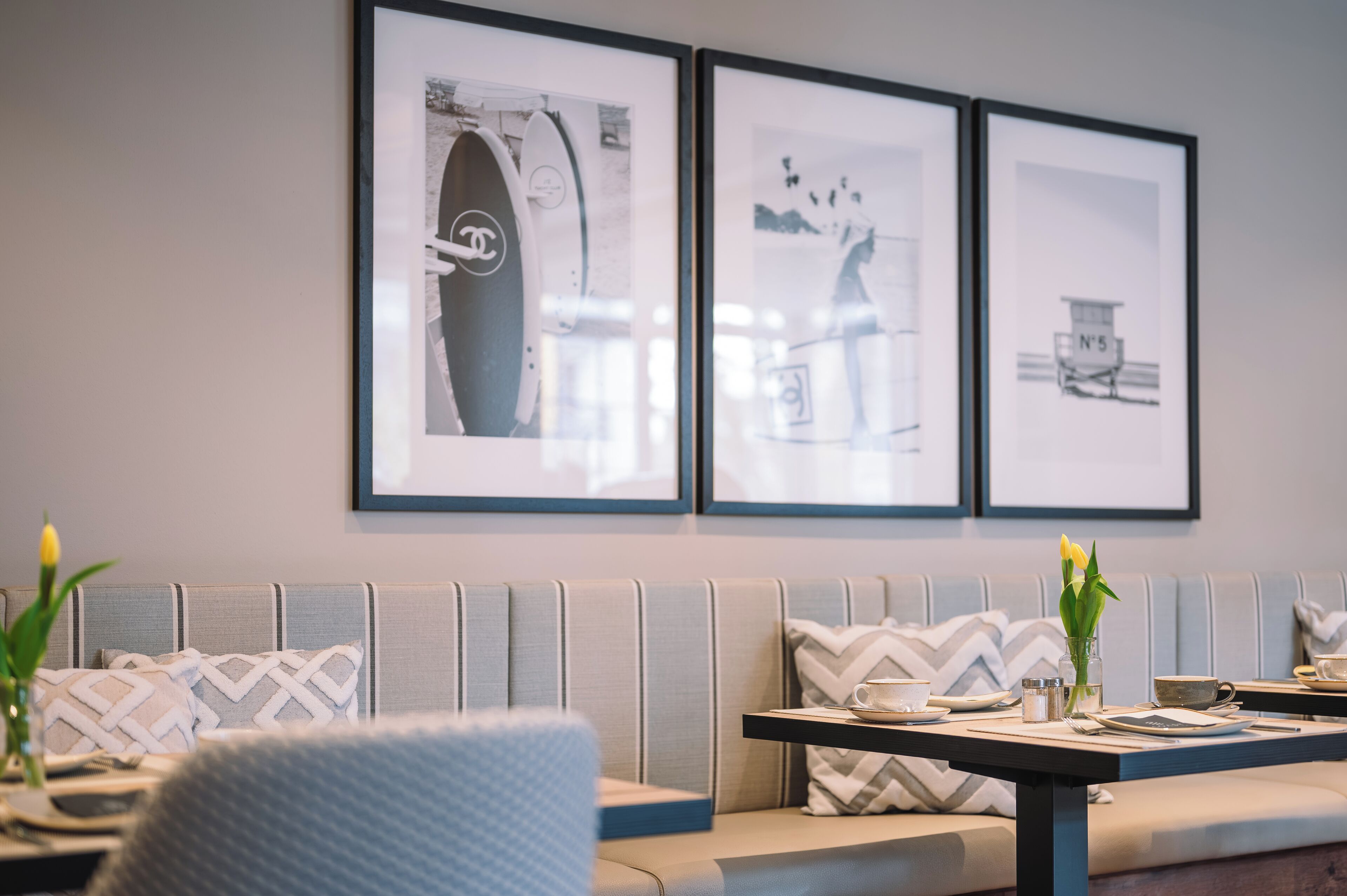Un espace repas moderne avec une longue table, des sièges rembourrés et des œuvres d’art encadrées accrochées au mur.