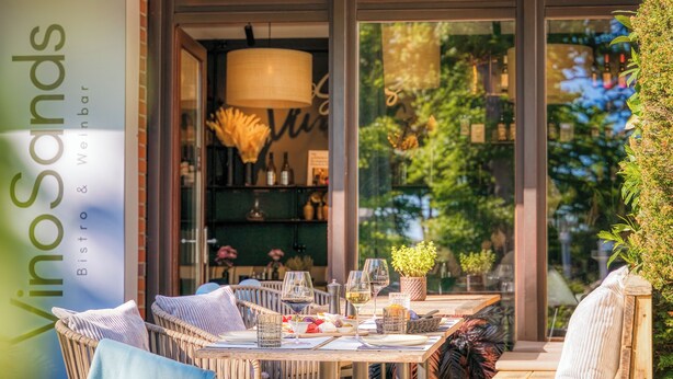 An outdoor dining area with wicker furniture, glassware, and a menu board. - Hotel Royal - Timmendorfer Strand (Timmendorfer Strand)