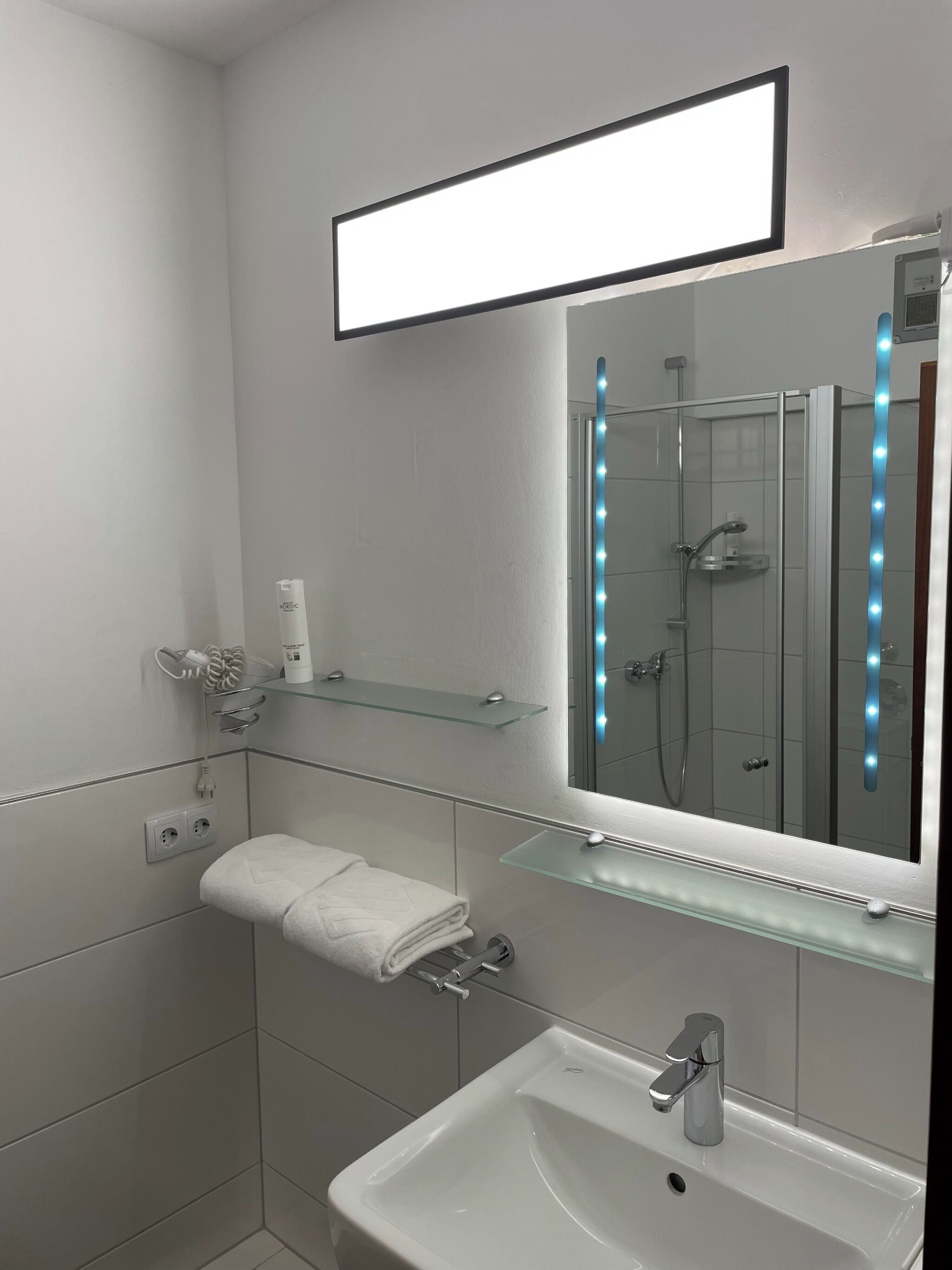 Ein modernes Badezimmer mit Duschkabine aus Glas, einem weißen Waschbecken und einem Spiegel mit LED-Beleuchtung.