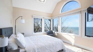A bedroom with a large bed, a chair, and multiple windows offering a view of the sea. - Coastal Retreat Waterfront, Deck, Awesome Views (Wading River)