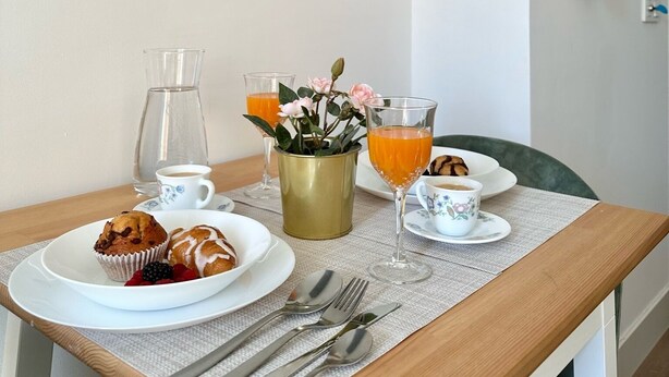 A breakfast setup with plates of food, glasses of orange juice, a pitcher of water, and a vase with flowers on a table. - Casa Secunda Romar (Córdoba)