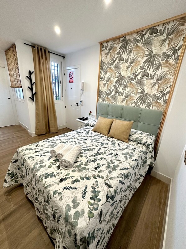 A bedroom with a floral bedspread, a green upholstered headboard, and a wooden headboard panel with a leaf pattern. - Casa Secunda Romar (Córdoba)