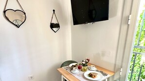 A dining area with a table set for two, a TV mounted on the wall, and a window with a view of greenery. - Casa Secunda Romar (Córdoba)