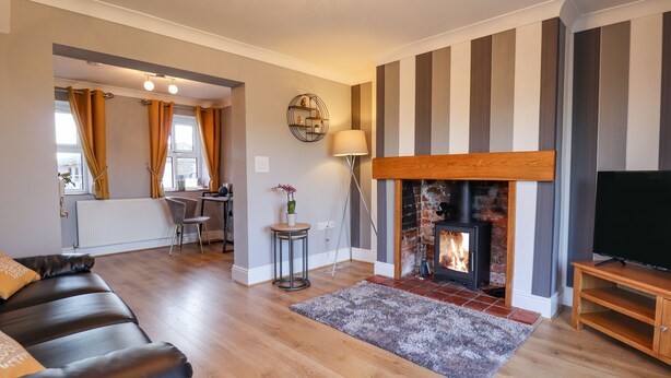 A living room with a fireplace, a sofa, a TV, and a dining area with a table and chairs. - Saddle Rack Cottage (Louth)