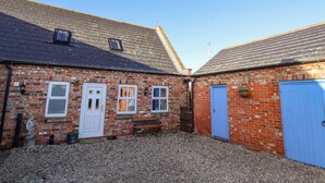 A brick building with a gravel driveway, a blue door, and a bench. - Saddle Rack Cottage (Louth)