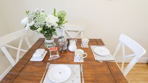 A dining table set with white plates, cups, and a teapot, surrounded by white chairs. - Saddle Rack Cottage (Louth)