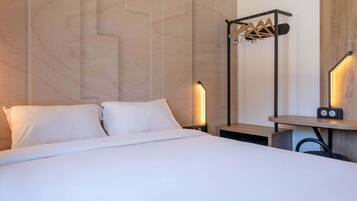 Ein Hotelzimmer mit einem Bett, einem Nachttisch, einer Wandlampe, einem Holzbodenregal und einem Kleiderhaken.