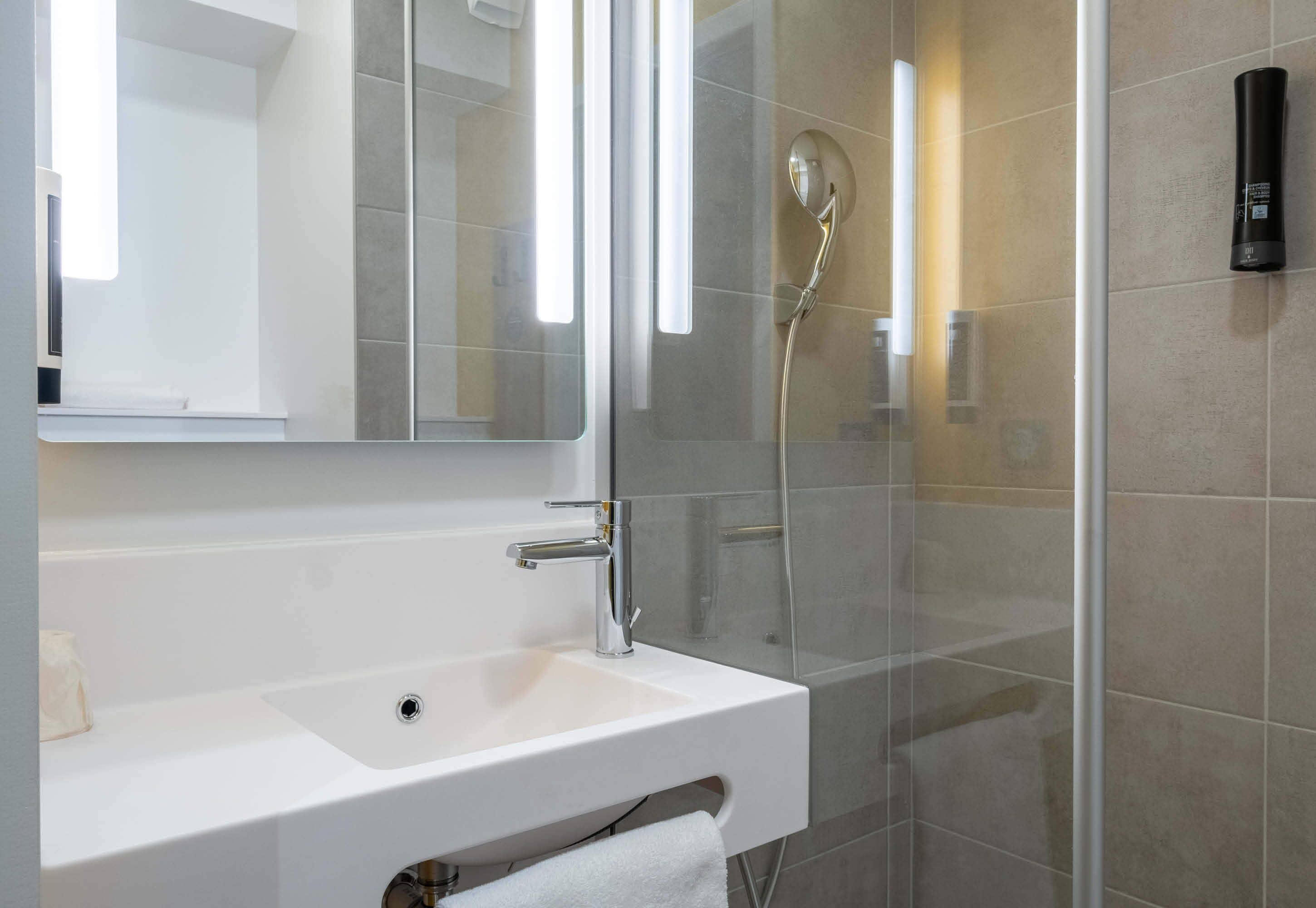 Un baño moderno con un lavabo blanco, un espejo y una zona de ducha con mampara de vidrio.