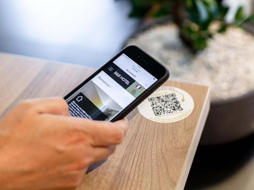 A smartphone displaying a hotel booking app interface with a QR code on a wooden surface.