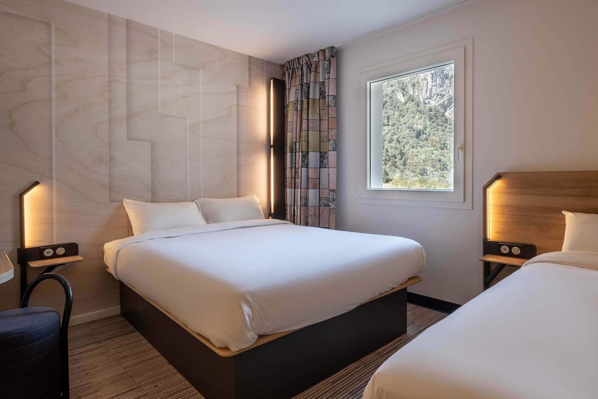 Habitación de hotel con una cama grande, dos mesitas de noche y una ventana con vistas a árboles.