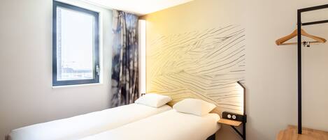 Una habitación de hotel con cama, ventana, una obra de arte en la pared y una silla de madera.