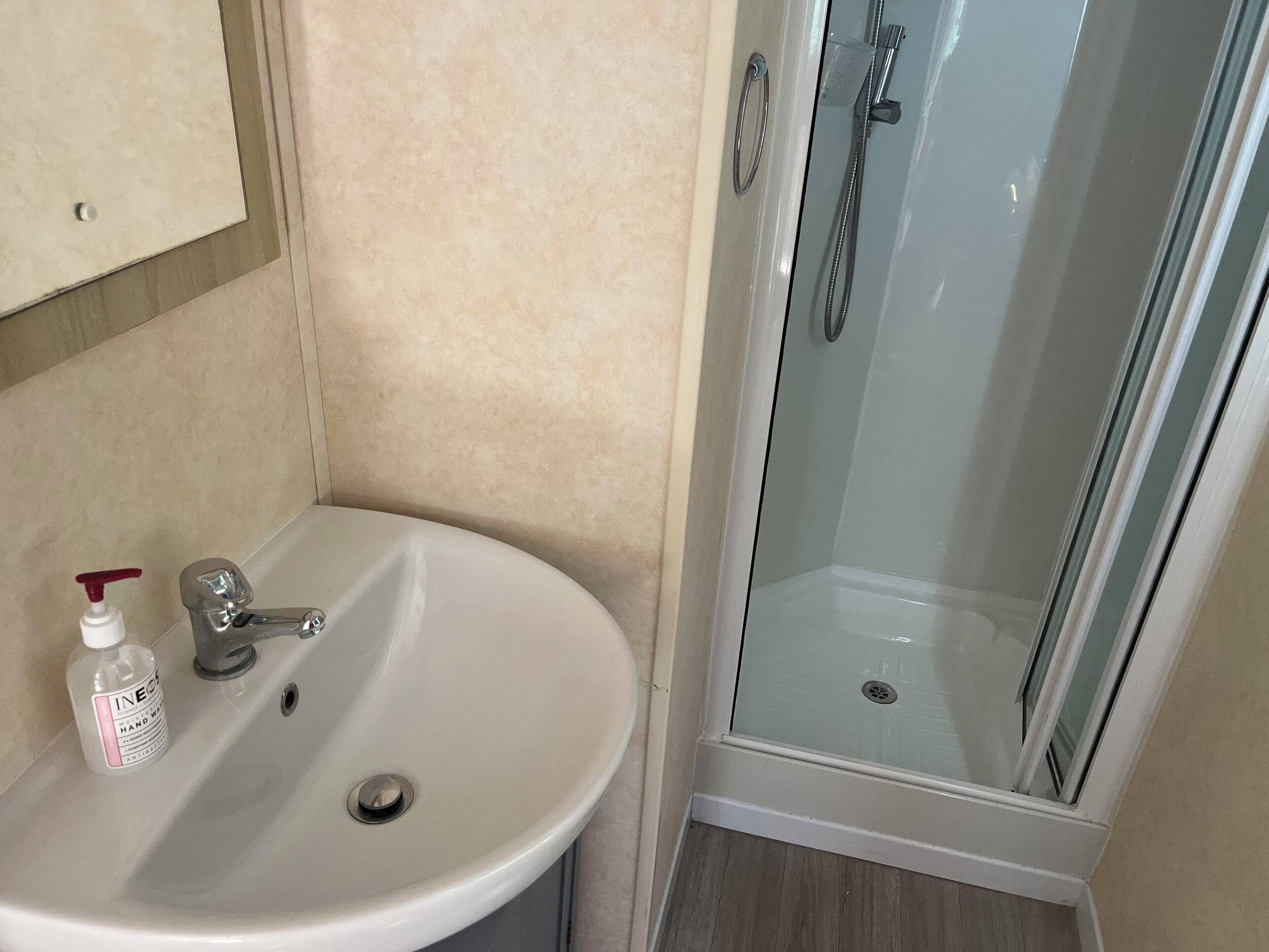 Ein Badezimmer mit Waschbecken, Handseifen-Spender und einer Duschkabine.