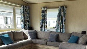 A cozy RV interior with a sectional sofa, a grey ottoman, and a grey carpet. - pet Free 2 Bedroom Caravan With Decking at Heacham (King's Lynn)