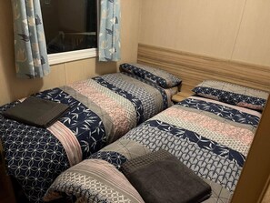 A twin room with two beds, patterned bedding, a window with curtains, and a wooden headboard.