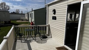 A covered outdoor deck with a table and chairs, a small rug, and a door leading to a covered area. - pet Free 2 Bedroom Caravan With Decking at Heacham (King's Lynn)