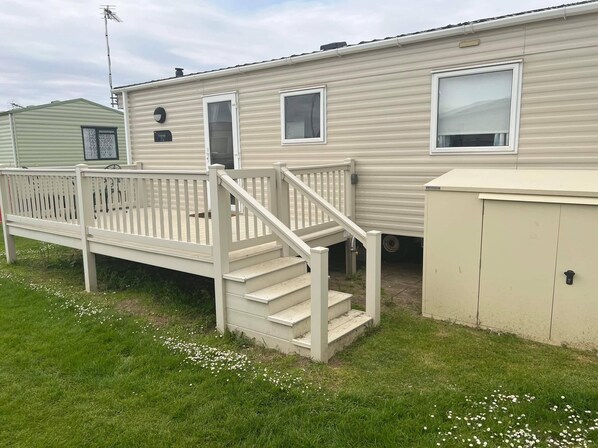 A mobile home with a front deck, a staircase, and a utility shed.