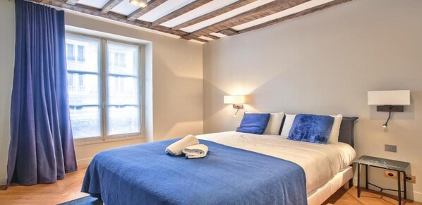 Une chambre à coucher avec un lit, une fenêtre, une table de chevet et une lampe fixée au mur.