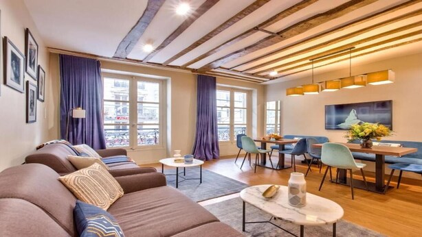 A modern living room with a sofa set, dining area, and large windows with curtains.