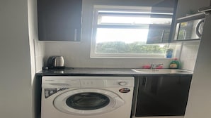 Cocina compacta con lavadora, microondas y ventana que proporciona luz natural.